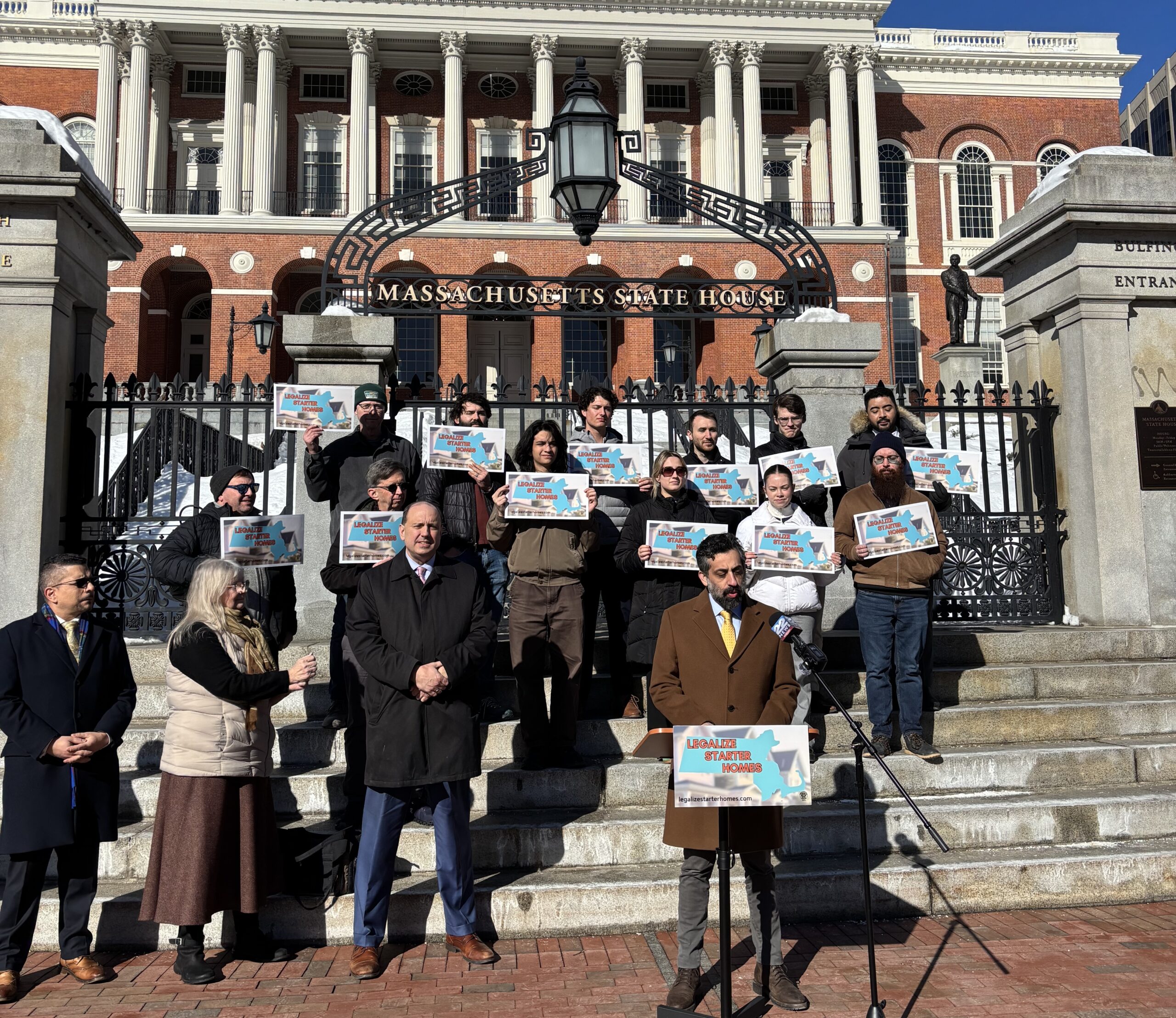 Jesse Kanson-Benanav speaking to a crowd of reporters with housing advocates holding signs behind him